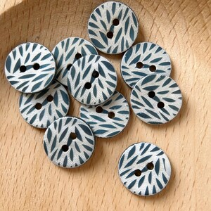 May include: A collection of ten round, two-hole buttons with a white background and a dark blue leaf pattern.