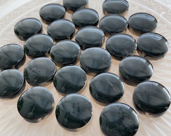 May include: A collection of twenty-one small, circular, black cabochons with a smooth, polished, and reflective surface. Each piece features a domed top and a flat base, arranged in a loose cluster. The objects appear uniform in size and shape.