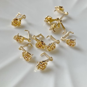 May include: A group of ten gold-tone rose-shaped metal charms with a loop on the back. The charms are ideal for adding a touch of elegance to jewellery projects.