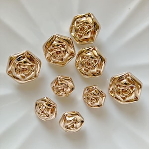 May include: A set of nine gold-toned rose-shaped buttons. The buttons are all different sizes and have a raised, textured design.