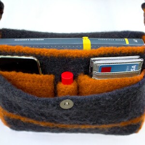 Pu&ograve; includere: Una borsa a tracolla in maglia a righe grigie e arancioni con chiusura a zip e bottone a pressione. La borsa &egrave; aperta e ha diverse tasche all'interno. Le tasche contengono un telefono, un taccuino, un rossetto e carte di credito.