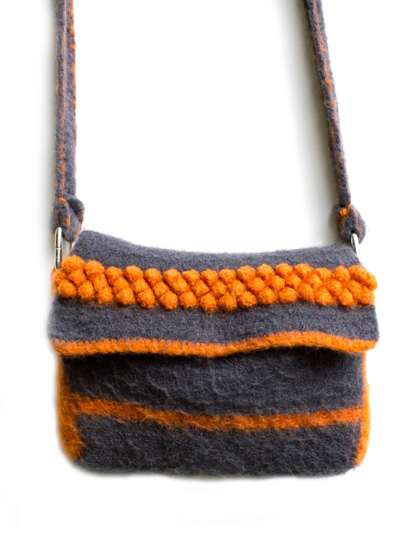 Pu&ograve; includere: Una borsa a tracolla in feltro grigio con una spessa tracolla e rifiniture in feltro arancione. La borsa ha una chiusura a lembo e una singola tasca sul davanti.
