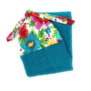 May include: A teal blue kitchen towel with a floral print fabric attached to the top. The floral print features red, pink, yellow, and blue flowers on a white background.