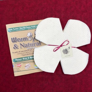 May include: A package of white needle-punched cotton batting in the shape of a flower. The package is tied with a red ribbon and a small tag that says "Warm & Natural Needled Cotton".