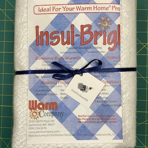 May include: White Insul-Brite batting with a blue ribbon. The label reads "Ideal For Your Warm Home® Pro" and "Insul-Brite". The label also lists the product's uses, including bedding projects, ski apparel, window shades, and more. The label also states "Not for Use in the Microwave!" and includes the company's name and contact information.