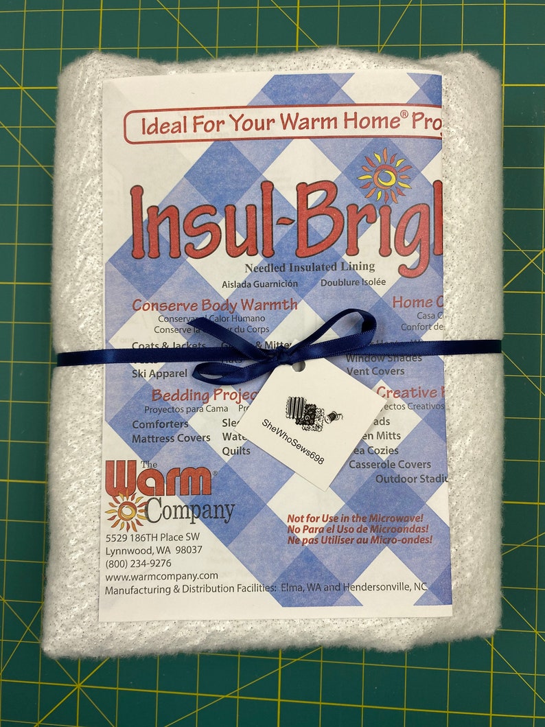 May include: White Insul-Brite batting with a blue ribbon. The label reads "Ideal For Your Warm Home&reg; Pro" and "Insul-Brite". The label also lists the product's uses, including bedding projects, ski apparel, window shades, and more. The label also states "Not for Use in the Microwave!" and includes the company's name and contact information.