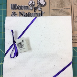 May include: A white needle-punched felt fabric square with a purple ribbon tied around it. The fabric is labeled "Warm & Natural" and has the text "Needle Punched - Does Not Contain Resins or Glues!" printed on it.