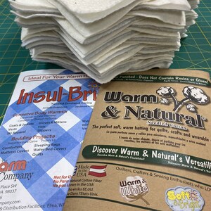 May include: A stack of white cotton batting, a brown and white brochure with the text "Warm & Natural Needled Cotton" and a blue and white brochure with the text "Insul-Bri Needled Insulated Lining".