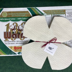 May include: Four white cotton guitar fretboard protectors tied together with a burgundy ribbon. The protectors are shaped like a flower with four petals. A small white tag with the text "SheKnowsSewing" is attached to the ribbon. The protectors are on a green surface with a white and gold package in the background. The package has the text "100% Natural Cotton ~ 100% Cotton Scrim" and "The Warm Company" printed on it.