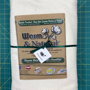 May include: A white cotton batting with a brown label that reads "Warm & Natural". The label says "Needle Punched - Does Not Contain Resins or Glues!" and "Discover Warm & Natural's Versatility!" The label also says "Made in the USA" and "100% Natural Cotton Fiber Grown in the USA".