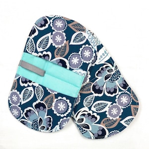 May include: A pair of teal oven mitts with a floral pattern in white, gray, and brown. The mitts have a light blue band with a gray loop for hanging. Kitchen textiles.