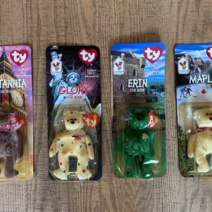 May include: Four Ty Beanie Babies in their original packaging. The beanie babies are Britannia the Bear, Glory the Bear, Erin the Bear, and Maple the Bear. Each beanie baby is wearing a different outfit representing a different country.