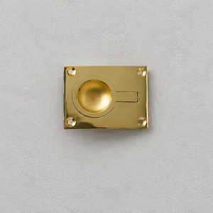 May include: Three rectangular brass flush pulls with a polished gold-tone finish. Each pull features a central circular recessed handle and four corner screw holes for mounting, designed for installation on cabinet doors or drawers.