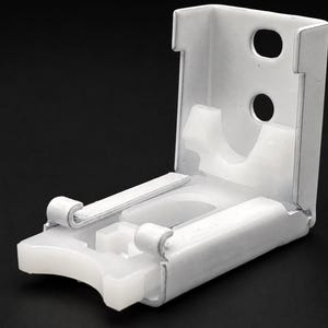 Puede incluir: Un soporte de montaje en L de metal blanco con un diseño articulado y una pieza de plástico translúcido. La placa trasera vertical incluye dos orificios circulares para tornillos, mientras que la base horizontal presenta un borde frontal curvo.