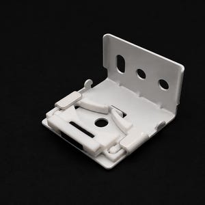 Puede incluir: Un soporte de montaje de metal blanco para persianas con un diseño en forma de L, que presenta una placa trasera vertical con tres orificios circulares y una placa base horizontal con un orificio central y un mecanismo de bloqueo de plástico.
