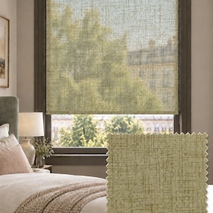 May include: A light olive green roller blind with a textured, cross-hatched fabric pattern installed in a window frame. A square fabric swatch with the same olive green cross-hatched design and pinked edges is positioned in the foreground.