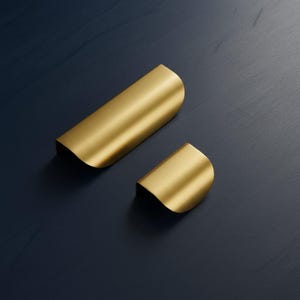 May include: Two gold-coloured metal cabinet pulls with a smooth, brushed finish. The larger pull is rectangular with rounded edges, while the smaller pull is a compact, semi-circular piece. Both hardware items feature a curved, ergonomic design.
