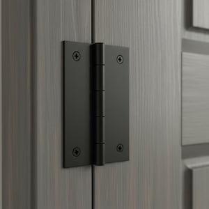 Puede incluir: Una bisagra de puerta de metal negro mate con un diseño de placa rectangular y un cilindro central. La bisagra está fijada a un marco de puerta de madera gris oscuro con cuatro tornillos de estrella negros a juego, ofreciendo un aspecto limpio.