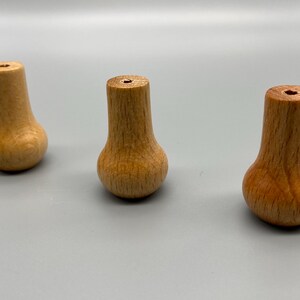 Könnte beinhalten: Drei hellbraune Holzknöpfe mit einem glatten, konischen, glockenförmigen Design. Jeder Knopf weist eine sichtbare natürliche Holzmaserung und ein kleines, zentriertes kreisförmiges Loch an der Oberseite auf und steht aufrecht in einer Reihe.