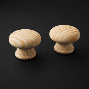 May include: Two round cabinet knobs made of light-coloured natural wood. Each knob features a smooth, mushroom-shaped top with visible wood grain patterns in shades of tan and cream, supported by a smaller, tiered circular base for mounting.