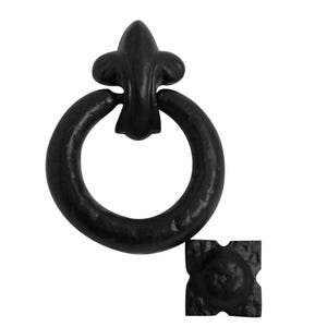 May include: A black metal ring pull handle featuring a fleur-de-lis top mount and a textured surface. The hardware includes a separate square-shaped mounting plate with a matching black finish and a hammered, uneven texture throughout.