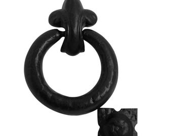 Könnte beinhalten: Ein schwarzer Ringgriff aus Metall mit einer fleur-de-lis-förmigen Halterung und einer strukturierten Oberfläche. Das Set enthält eine separate quadratische Montageplatte mit passender schwarzer Oberfläche und Hammerschlagoptik.