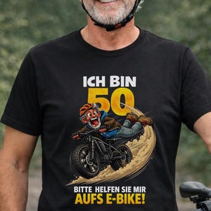 Puede incluir: Un hombre con una camiseta negra con el texto "ICH BIN 50" y un gráfico de una persona en una bicicleta eléctrica. La camiseta también tiene el texto "BITTE HELFEN SIE MIR AUFS E-BIKE!". Lleva un casco amarillo y gafas de sol.