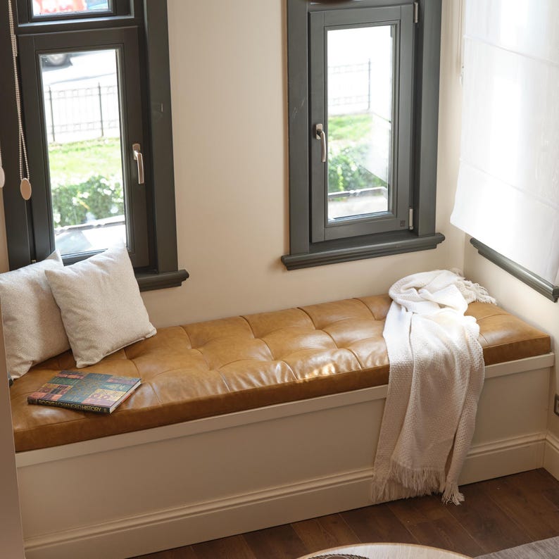 Large window seat leather cushion arranged in a bright reading nook with elegant minimalist décor.