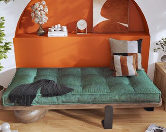 May include: A low-profile daybed featuring a tufted emerald green fabric cushion on a wooden frame with a black metal leg. A black fringed throw blanket rests on the cushion, accompanied by two square throw pillows with geometric patterns.