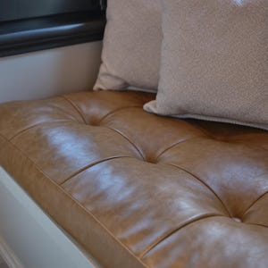 Custom tufted leather cushion displayed on a wooden bench in a modern living room with warm tones.