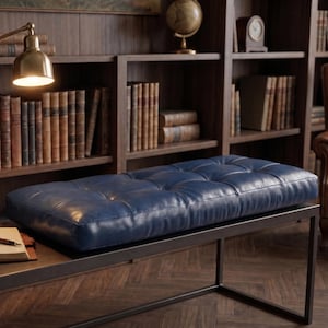 May include: A rectangular navy blue leather bench with a tufted button design and a smooth, matte finish. The bench features a sleek, black metal frame with a minimalist base structure, providing a sturdy foundation for the cushioned seat.