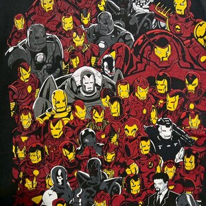 May include: Black t-shirt featuring a collage of Iron Man illustrations in various poses and armor designs. The artwork showcases Iron Man's iconic red and gold color scheme, along with gray and black variations. The words "IRON MAN" are at the bottom.