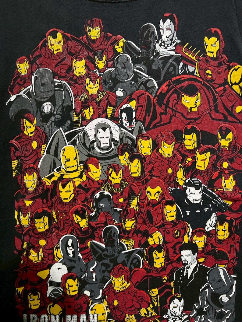 May include: Black t-shirt featuring a collage of Iron Man illustrations in various poses and armor designs. The artwork showcases Iron Man's iconic red and gold color scheme, along with gray and black variations. The words "IRON MAN" are at the bottom.