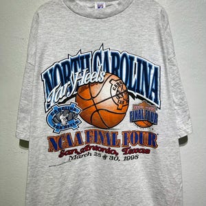 May include: A gray t-shirt featuring the text "North Carolina Tar Heels" above a basketball graphic. The shirt also displays "NCAA Final Four" and "San Antonio, Texas, March 28 & 30, 1998."
