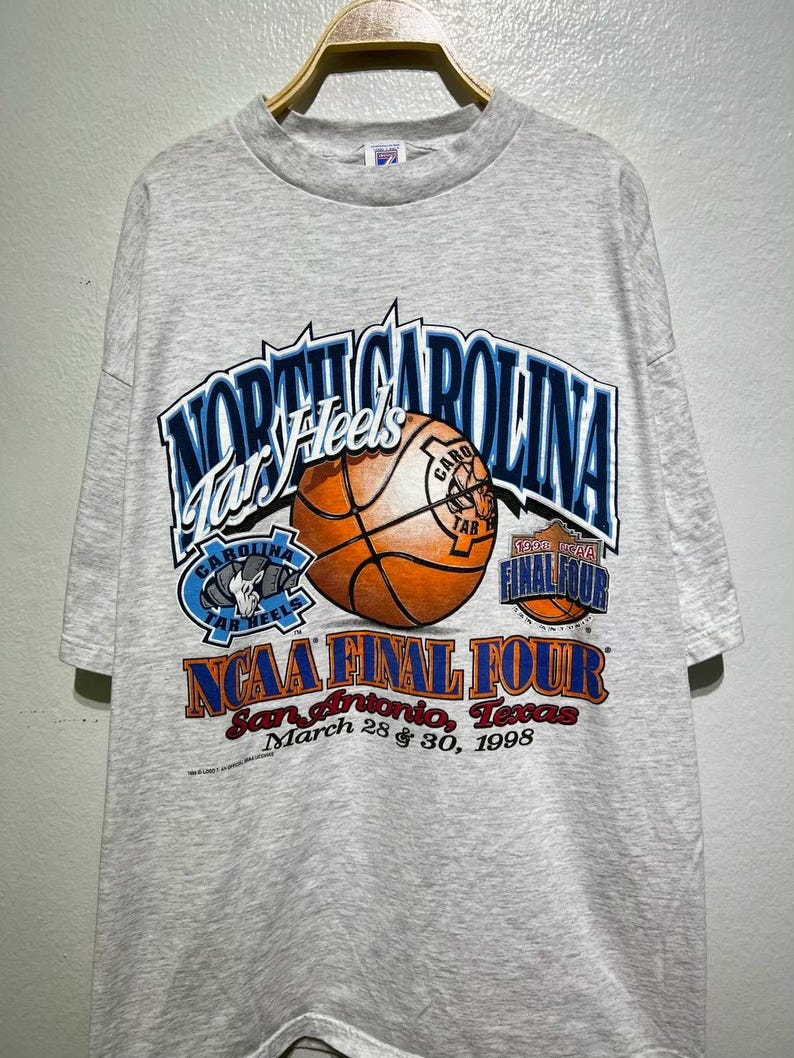 May include: A gray t-shirt featuring the text "North Carolina Tar Heels" above a basketball graphic. The shirt also displays "NCAA Final Four" and "San Antonio, Texas, March 28 & 30, 1998."