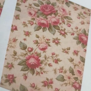 May include: A floral pattern featuring pink roses and green leaves on a cream-colored background. The design has a vintage, romantic aesthetic, with a repeating pattern of roses and smaller floral elements.