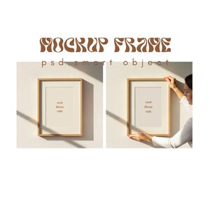 May include: Two wooden picture frames with a white mat and blank interior are displayed on a light-colored wall. The text "MOCKUP FRAME" and "YOUR DESIGN HERE" are visible. One frame is being held by a person.
