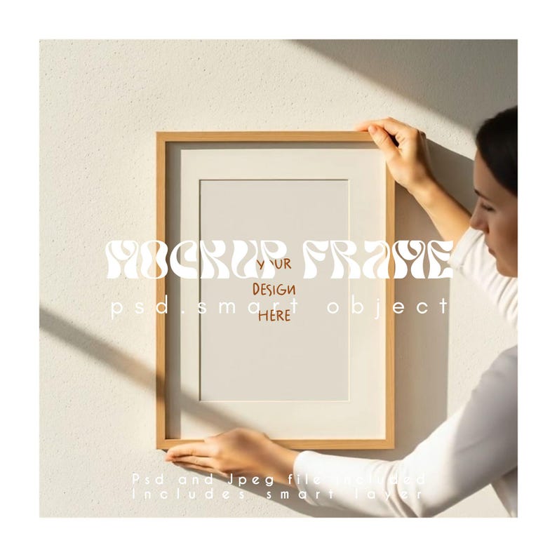 May include: A wooden picture frame with a white mat and a blank interior. The frame is held by a person against a textured white wall. The frame has the text "MOCKUP FRAME" and "DESIGN HERE" on it.
