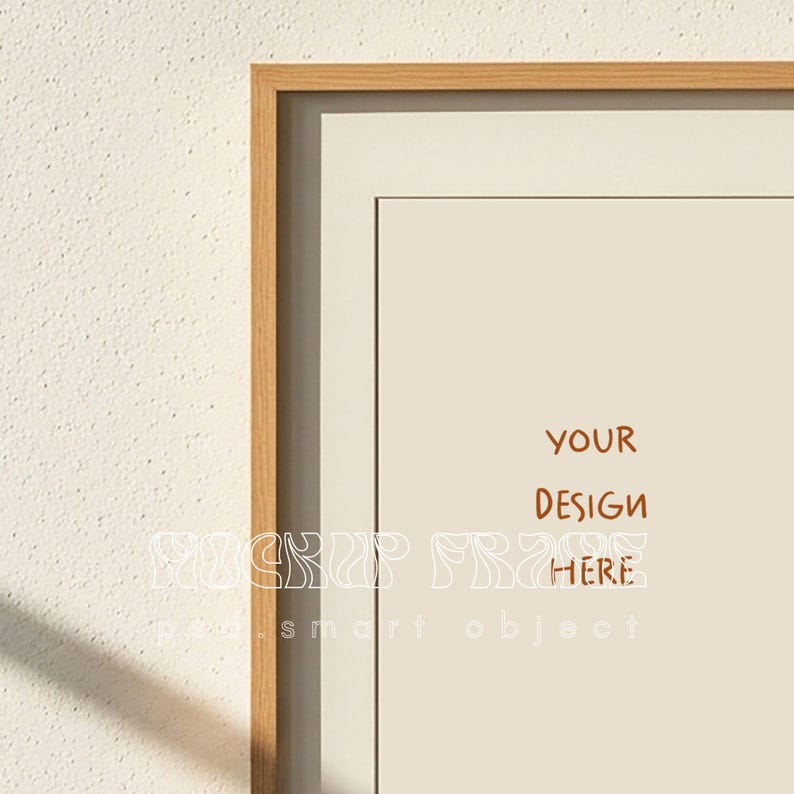 May include: A framed print mockup with a light wood frame and a cream-colored mat. The print features the text "YOUR DESIGN HERE" in a brown font. The background is a textured off-white wall.