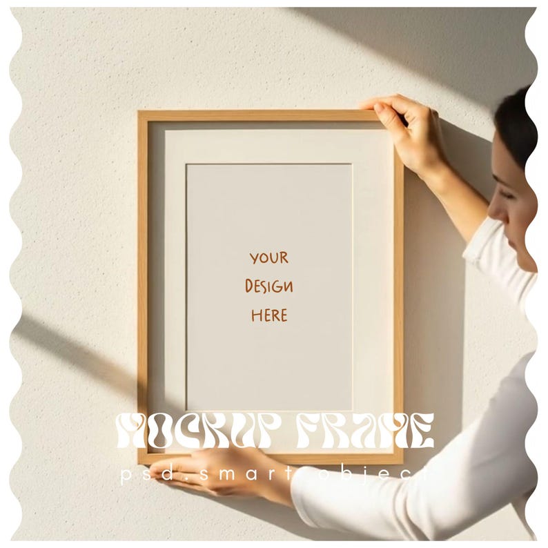 May include: A rectangular wooden picture frame with a white mat and a blank white space that reads "YOUR DESIGN HERE". The frame is being held up against a white wall. The words "MOCKUP FRAME" and "psd smart bies" are written at the bottom of the frame.