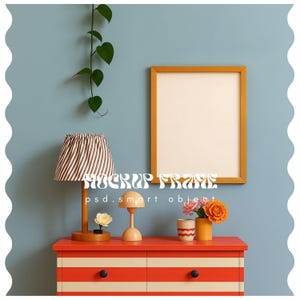 Puede incluir: Un marco de presentación dorado se muestra sobre una cómoda roja con rayas blancas. Una lámpara a rayas, una pequeña lámpara de mesa y flores en un jarrón están sobre la cómoda. El texto "MOCKUP FRAME" y "psd.smart object" son visibles.