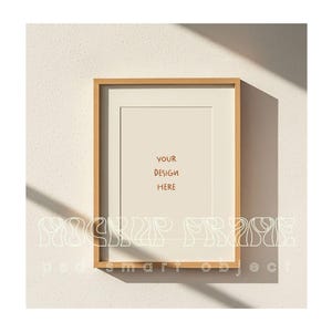 May include: A rectangular wooden picture frame with a white mat, hanging on a textured white wall. The frame contains the text "YOUR DESIGN HERE" in brown. The words "MOCKUP FRAME" and "podsmart object" are also visible.