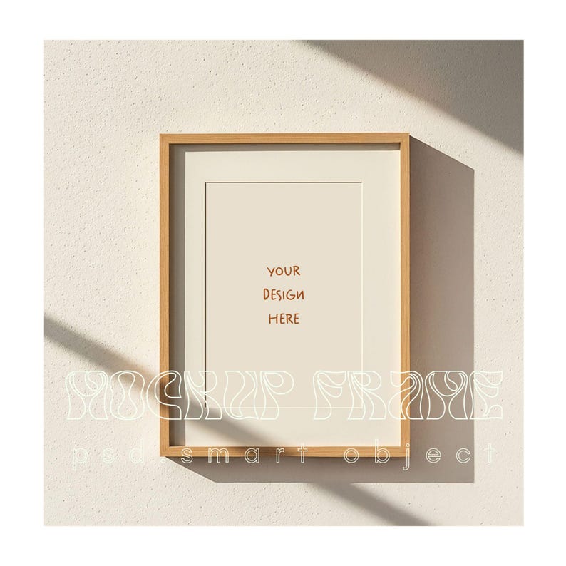 May include: A rectangular wooden picture frame with a white mat, hanging on a textured white wall. The frame contains the text "YOUR DESIGN HERE" in brown. The words "MOCKUP FRAME" and "podsmart object" are also visible.