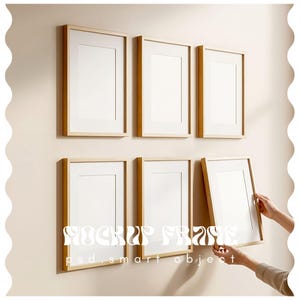 May include: Six rectangular picture frames with light wood-colored frames and white matting are mounted on a beige wall. One frame is being held by a person. The text "MOCKUP FRAME" and "psd.smart object" is visible on the bottom of the image.