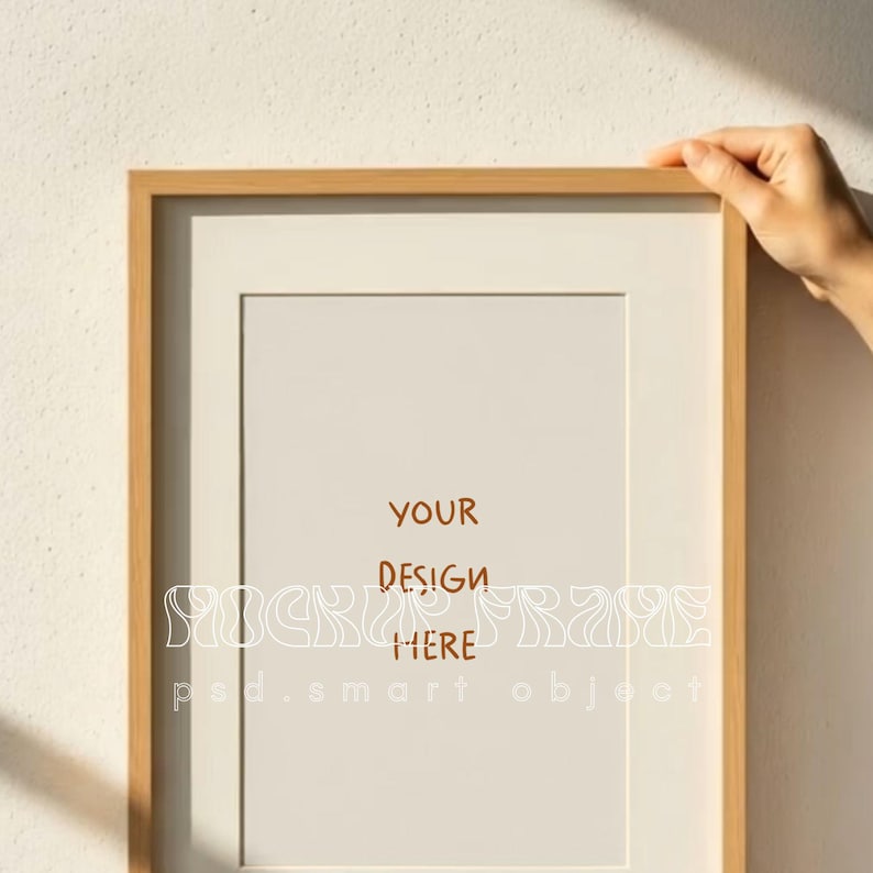 May include: A rectangular wooden picture frame with a white mat and a blank beige interior. The frame is held by a hand. The text "YOUR DESIGN HERE" is printed on the interior.