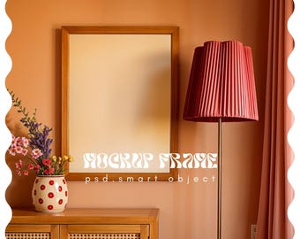 May include: A wooden framed mirror hangs on a peach-colored wall above a wooden cabinet. A red pleated lampshade stands on a gold pole. A vase with flowers sits on the cabinet. The text "MOCKUP FRAME" is displayed on the mirror.