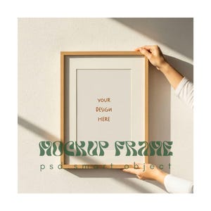 May include: A rectangular wooden picture frame with a white mat, held by a person. The frame has the text "YOUR DESIGN HERE" and "MOCKUP FRAME psd smart object" in green.