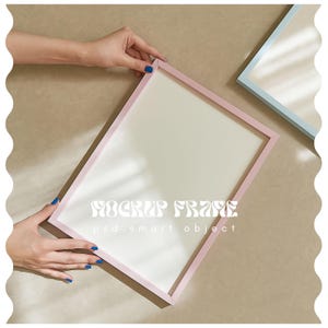 May include: A pink rectangular picture frame with a white interior, held by hands with blue nail polish. The text "MOCKUP FRAME" and "psd. smart object" are printed on the frame. A light blue frame is visible in the background.