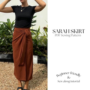 May include: A woman wearing a black t-shirt and a brown wrap skirt. The skirt is tied at the waist with a long sash. The text "SARAH SKIRT PDF Sewing Pattern" is displayed above the image. The text "Beginner friendly & Sew along tutorial" is displayed below the image.