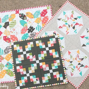 Può includere: Una collezione di trapunte fatte a mano con vari motivi geometrici. Le trapunte presentano un mix di tessuti colorati, tra cui pois, righe e stampe floreali. Ogni trapunta ha un bordo a contrasto con un motivo a righe rosse e bianche.